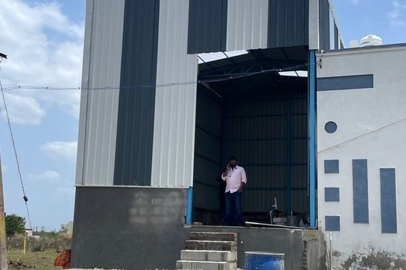 Tall single-bay structure clad in colour-coated profile sheeting tied into an existing plant building