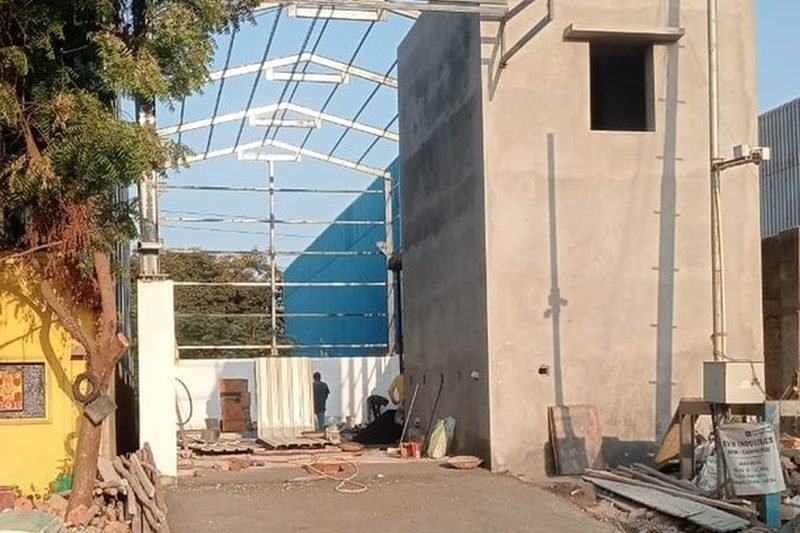 Portal columns and rafters with tubular purlin grid being erected alongside an RCC utility block