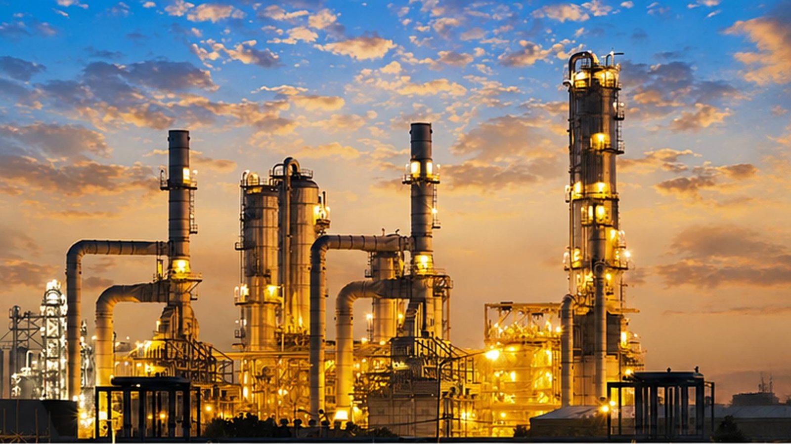 Refinery columns and process piping lit against a dusk sky — the kind of plant LKS Industries supplies strainers, valves and vessels into