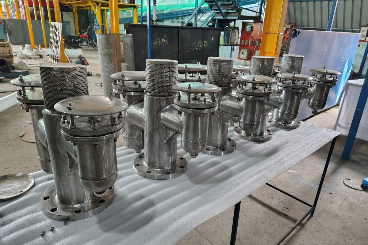 Row of stainless steel air release valves with flanged bases and perforated cowls awaiting inspection